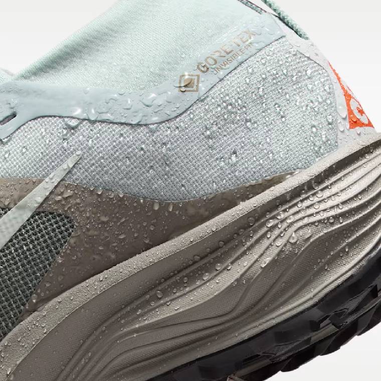 Детайлен изглед на петата на дамски маратонки Nike Pegasus Trail Gore-Tex в сиво с оранжеви елементи с водна защита и лого Gore-Tex Invisible Fit 